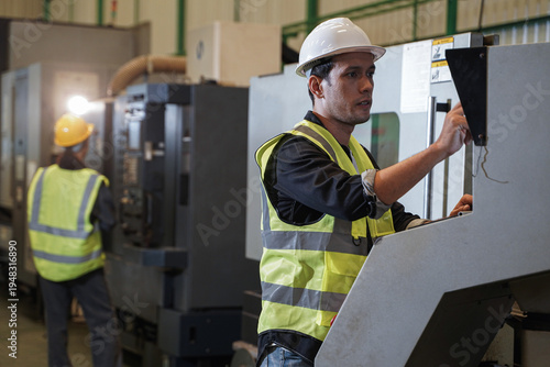 Australian male engineer and Asian female engineer collaborating on CNC machine operation and technical data analysis using a laptop on the factory floor.