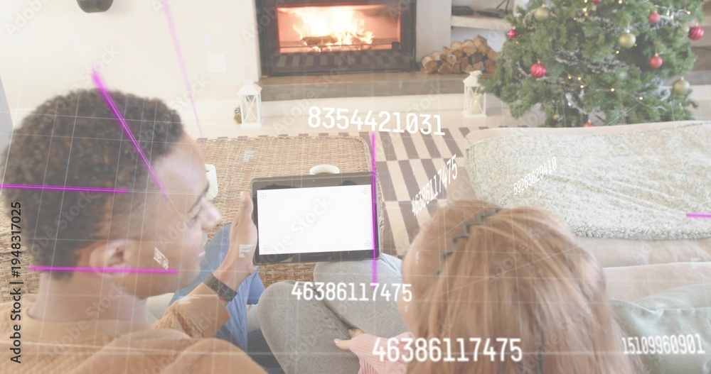 Naklejka premium Couple sitting closely on couch by fireplace in living room, holding tablet, viewing augmented grid