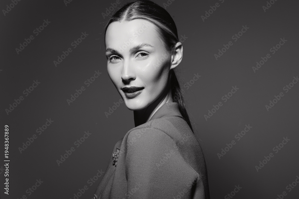 Fototapeta premium Portrait of a white woman with pale skin and sleek hairstyle wearing textured clothing on dark background. Concept of fashion, elegance, and monochrome beauty.