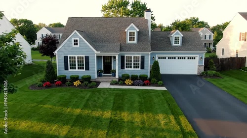 Light blue suburban home with manicured lawn, driveway, and surrounding greenery