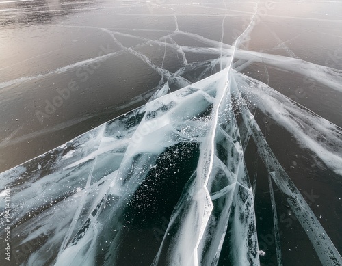 Cracked ice surface over clear lake water, featuring natural fracture patterns with sharp lines contrasting against the transparent water below. climate change
