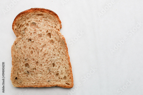 Single slice of whole grain bread rests on clean white surface