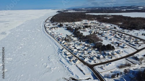 Aerial footage of Saint-Ulric-de-Matane in Gaspe Peninsula. Discover a picturesque snow-covered coastal village bordered by the frozen Saint Lawrence River.
