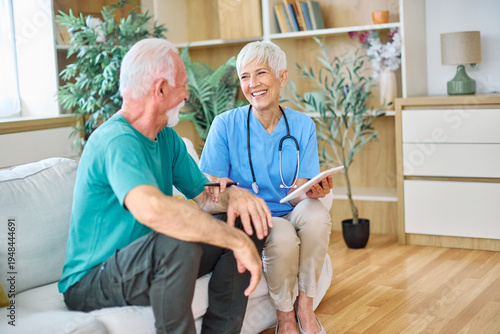 Doctor or nurse caregiver showing a tablet screen to  senior man at home or nursing home