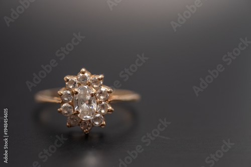Vintage gold ring with oval-cut clear gemstone surrounded by small diamonds, photographed on a dark background. Classic fine jewelry, engagement or heirloom accessory concept.