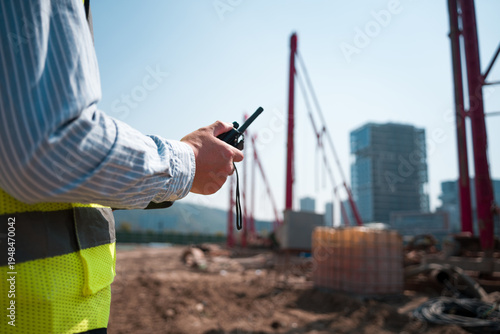 Foto Construction worker holding walkie-talkie directing site operations at a buildin