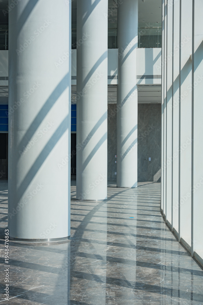 Fototapeta premium Modern architectural interior with white cylindrical columns and dramatic light shadows in a corridor