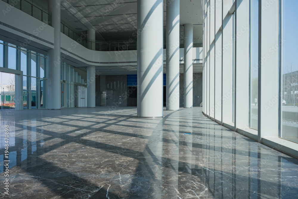 Fototapeta premium Modern architectural lobby with marble floor, columned arcade, and dramatic light shadows