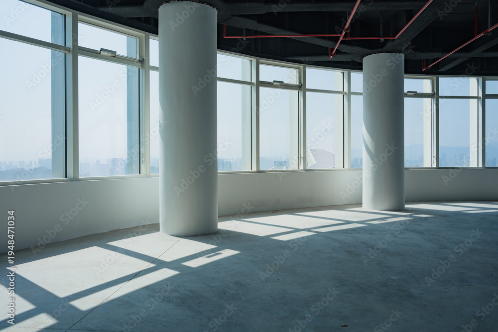 Obraz premium Spacious empty office interior with floor-to-ceiling windows, concrete columns, and dramatic light shadows