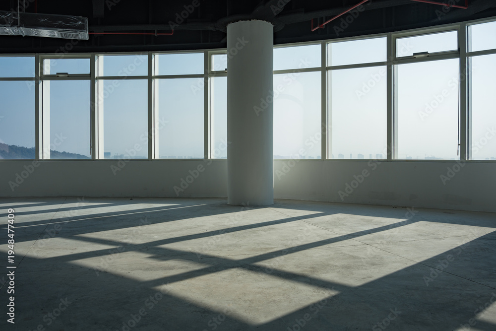 Fototapeta premium Empty modern office space with floor-to-ceiling windows casting geometric shadows from a central column
