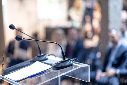 Fotografie Microphones in focus, unrecognizable people in background at business conference