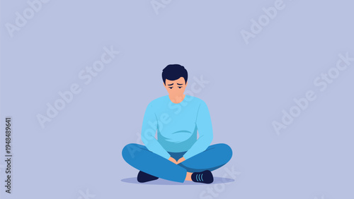 Sad young man sitting alone on the floor in a cross legged position feeling lonely and depressed with head down.