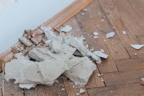 Fotografie Broken plaster debris scattered on wooden parquet floor near baseboard showing renovation demolition scene with dust and rubble fragments in beige tones