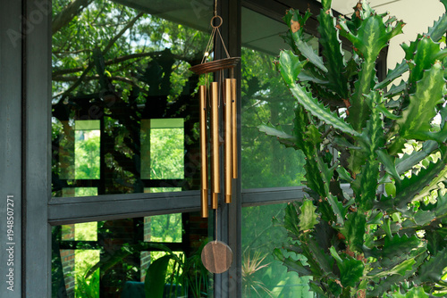 Billede på lærred Brass wind chime hanging next to a large succulent plant on a balcony next to a