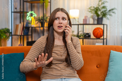 Foto Young woman at home argues on smartphone frowns raises voice uses sharp hand moves and speaks fast