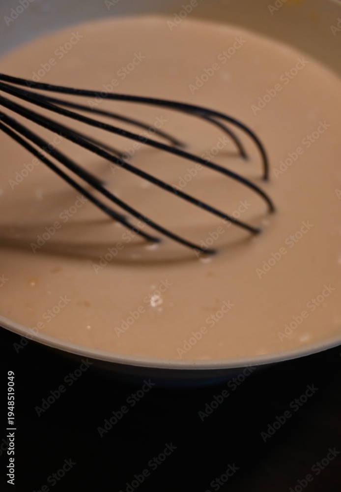 Fototapeta premium Close-up of pancake batter being mixed with a whisk in bowl. Conceptual food image representing homemade cooking, traditional dessert preparation and family kitchen concepts.