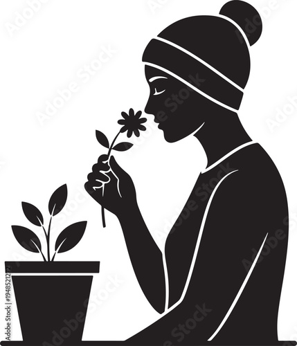 Black and white silhouette of a young woman wearing a beanie hat and smelling a small garden flower