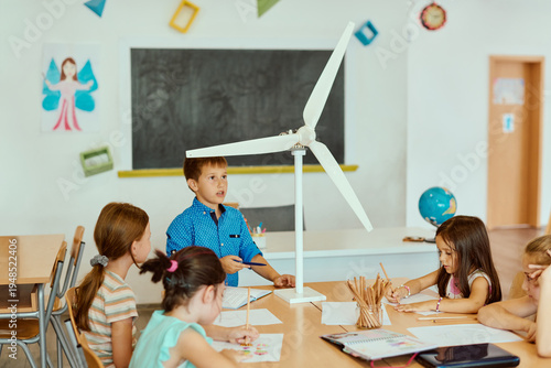 Children in a classroom presenting a wind turbine model during a school science project on renewable energy