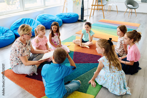 Obraz na płótnie Teacher reading a story to children during circle time in a colorful preschool c