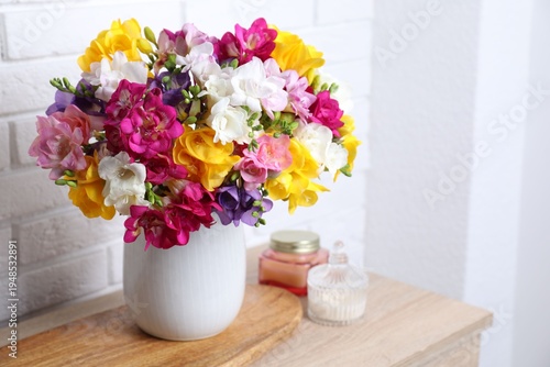 Photos Beautiful freesia flowers in vase and candles on wooden table near white brick wall indoors, closeup