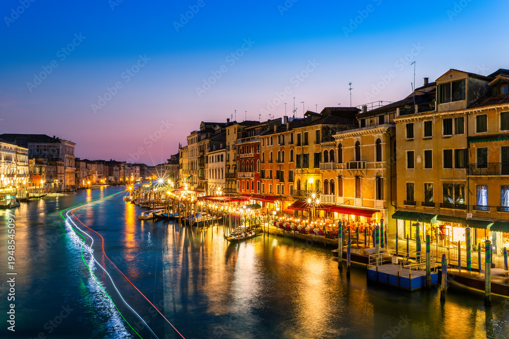 Naklejka premium Long exposure of Grand Canal at dusk as viewed from Rialto bridge, Venice, Italy. Boats leave light trails forming the colors of the Italian flag.