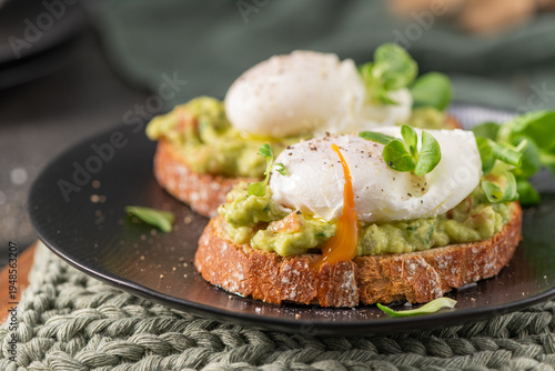 A tempting close up of avocado toast topped with a poached egg featuring a perfectly runny golden yolk, garnished with fresh microgreens and black pepper on a rustic sourdough slice