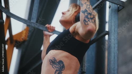 Tattooed Athletic Woman Doing Pull-Ups on Industrial Metal Ladder at Harbor Waterfront