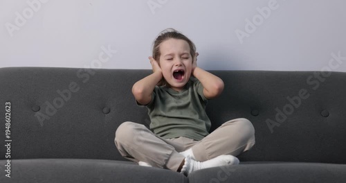 Autism. Little girl with sensory issues screaming on sofa indoors