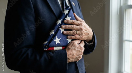 Close up of a senior male veteran in a suit holding a folded American flag over his heart. Solemn tribute and remembrance on Memorial Day