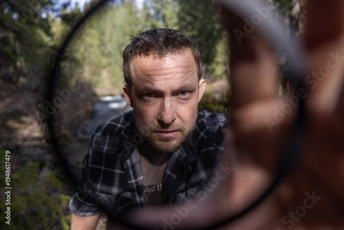 Man looking intently towards the camera thought a filter he hold and places over the lens