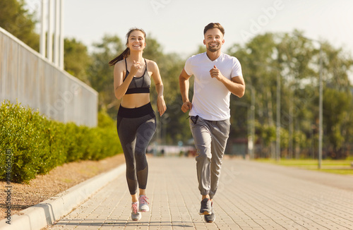 City road running and sport exercises of active couple, morning training and jogging of two happy strong runners. Young fit smiling woman and man running marathon. High motivation, workout concept