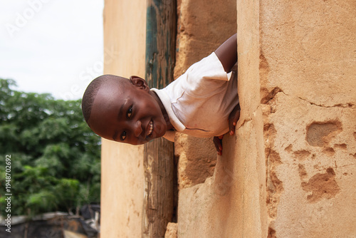Foto A young African boy sits quietly beside a crumbling wall in a Namibian refugee camp