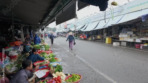 HUE, VIETNAM – 22 November 2025: Vendors prepare and sell fresh produce at a local market in Dong Ba Market. A shopper walks along the street.