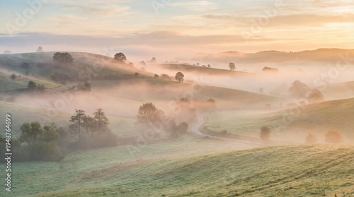A scenic summer sunrise glows over a misty mountain landscape and river, illuminating green hills, grassy meadows, and a winding countryside road under a cloud-filled sky