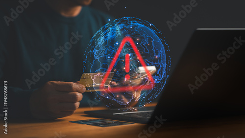 Man holding credit card at laptop with red warning sign and digital globe. Alert for cyber security threat, online banking fraud, payment error, and global network scam.