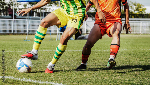 Close up sports action of football players competing for control of the ball on green field, highlighting powerful legs, athletic performance, outdoor competition