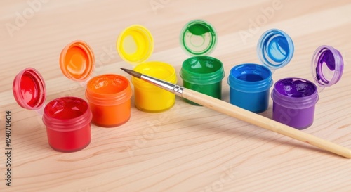 Assortment of colorful paint pots and a single brush laid out on a wooden surface, ready for artistic creation.