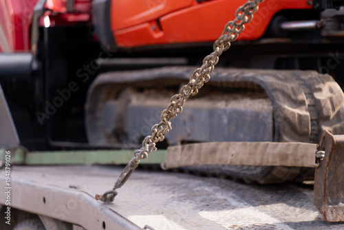 Foto Steel securing chain fastened across a compact tracked machine on a flatbed truc