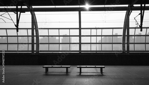 Two empty benches at train station platform with misty city skyline in black and white