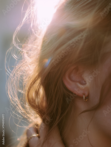 Close-up of a woman's ear, jeweled earring, and jawline with soft, golden backlighting