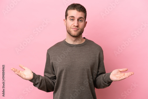 Young caucasian man isolated on pink background having doubts
