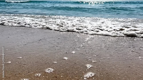 Waves gently wash onto a serene beach shore with smooth sand