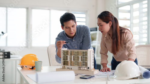 Asian adult male architect female engineer discuss building model design blueprints office workspace professional project planning construction development infrastructure