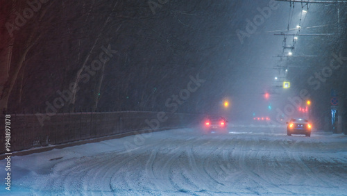 Cars driving along an evening winter city street during a snowstorm