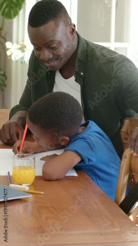 Vertical video: Leaning son, green-shirt dad guiding hand with red pencil at home learning