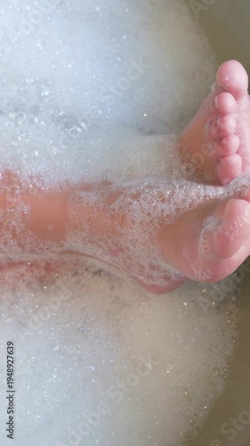 Vertical video: Reacting to water, small child feet wiggling in bathtub, bubbles clinging