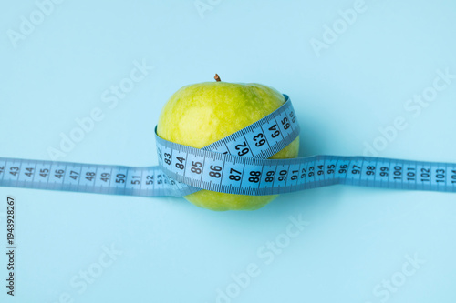 Concept of diet, healthy lifestyle, weight loss, fitness. Ripe green apple and blue measuring tape on blue background, flat lay top view. Space for text. Centimeter for tracking body measurements