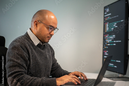 Male programmer wearing glasses works late at night with green code reflecting on his lenses focusing on software development coding and cybersecurity analysis.
