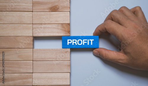 Hand placing wooden block with word profit to complete gap in business blocks representing financial success, business growth, revenue increase, strategic planning and profitability concept.