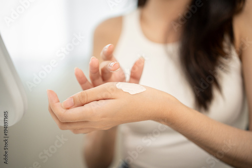 Beautiful woman applying skincare cream on smooth glowing face, smiling in mirror with confidence in routine. Apply cream to her cheeks to natural beauty, healthy skin.